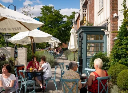 Groups of people sat under sun umbrellas outside a traditional pub