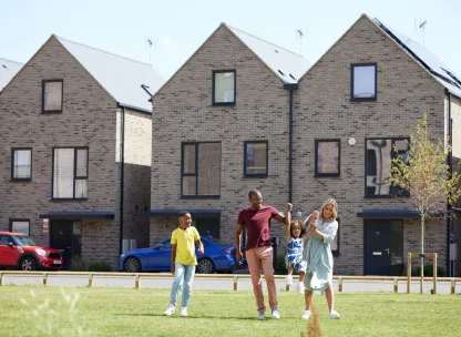 Family with two children playing on a green space in front of new build home