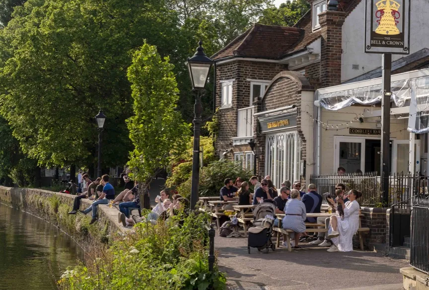 People sat on picnic benches outside a traditional pub by the river