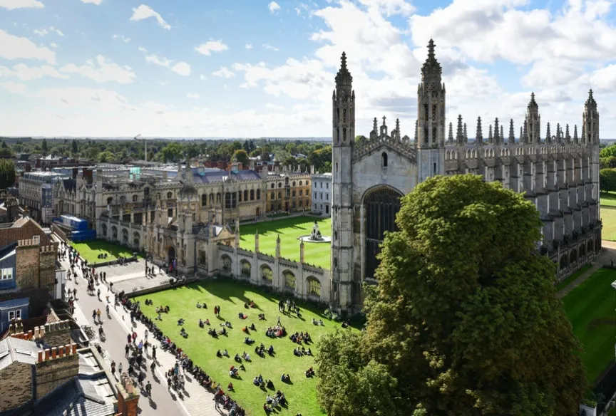Aerial view of Cambridge university surrounded by people sat on the fields