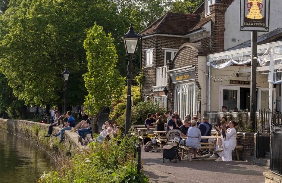 People sat on picnic benches outside a traditional pub by the river