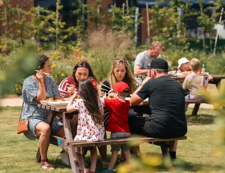 Family sat on a picnic bench in the sun eating lunch