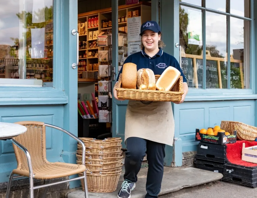 Smiling baker holding loaves of bread and stood outside local store